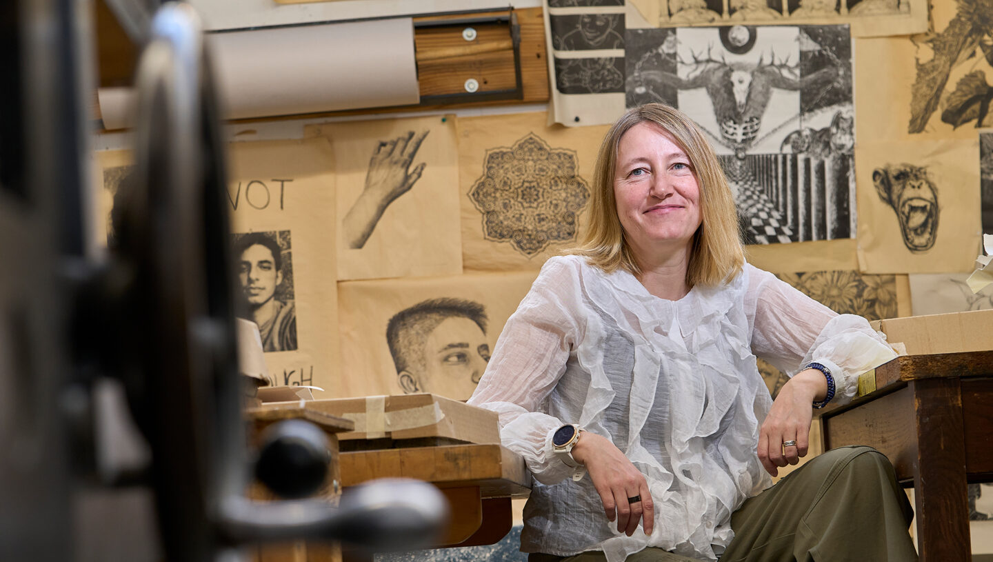 Environmental portrait of Linda O'Keeffe in a printmaking studio, surrounded by art prints.