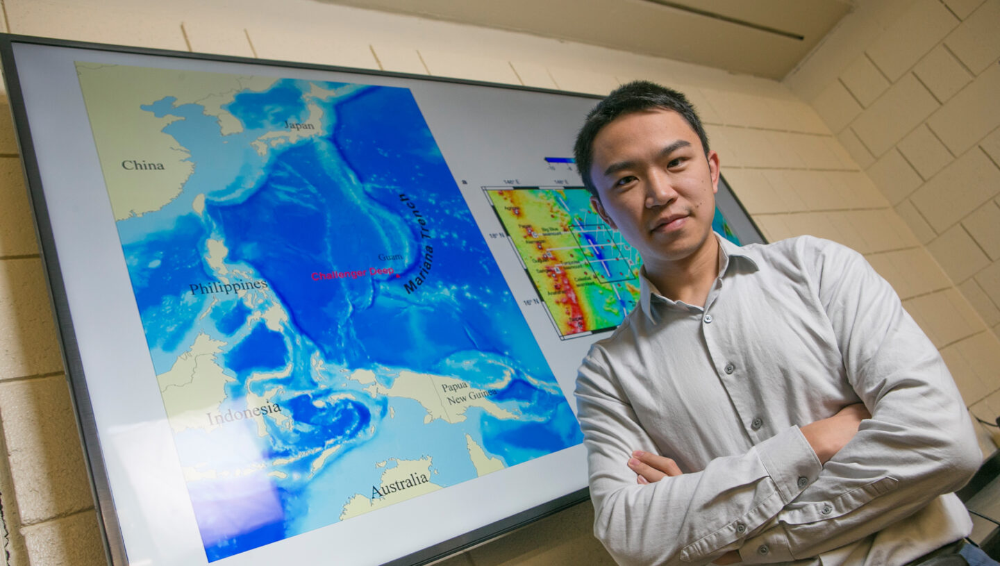 Environmental portrait of Weisen Shen standing against a screen showing climate data.