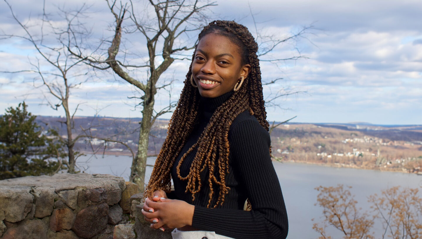 Environmental portrait of Rachel Alexandre with a water view and trees behind her.